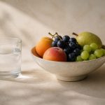 Glass of water beside fresh fruit bowl - illustration for How small daily habits shape your health in the next decade