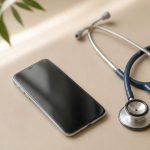 Smartphone beside stethoscope on table - illustration for Telemedicine vs In-Person Visits: Which Is Right for You?
